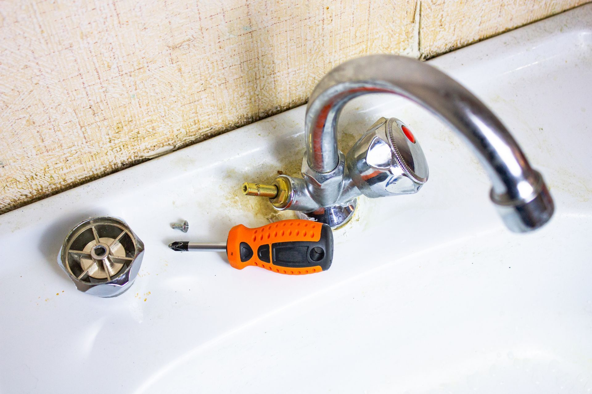 Faucet being repaired with screwdriver on a white sink.