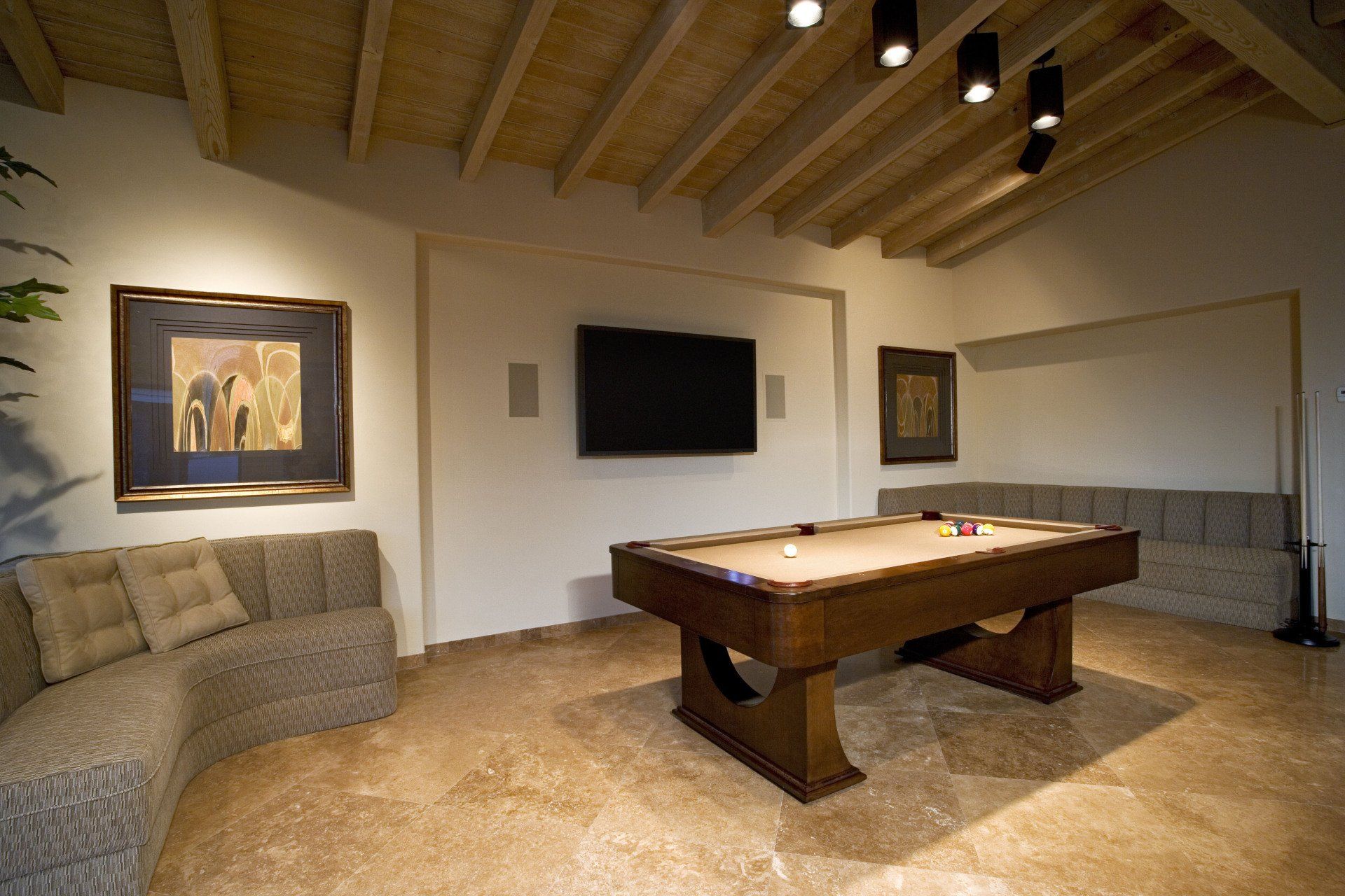 Pool table in a room with a TV, artwork, seating, and a wood ceiling.
