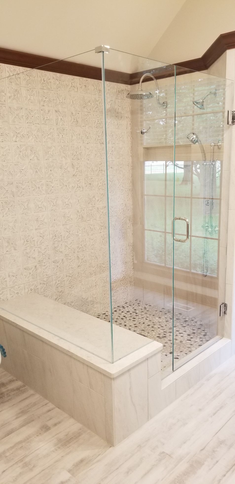 Spacious shower with stone tiles, glass walls, a bench, and a window.