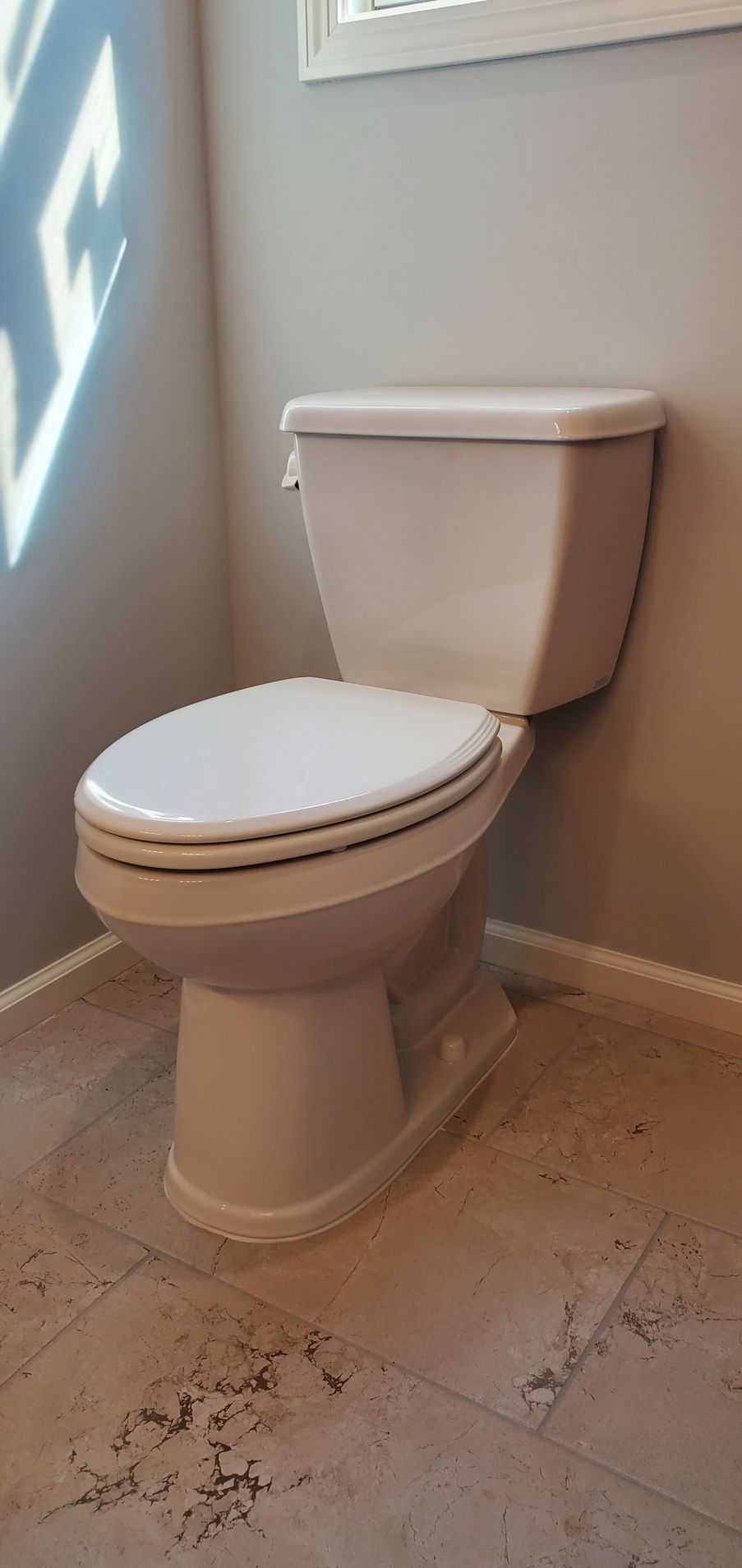Toilet in a light-colored bathroom. White toilet with closed lid against a pale grey wall.