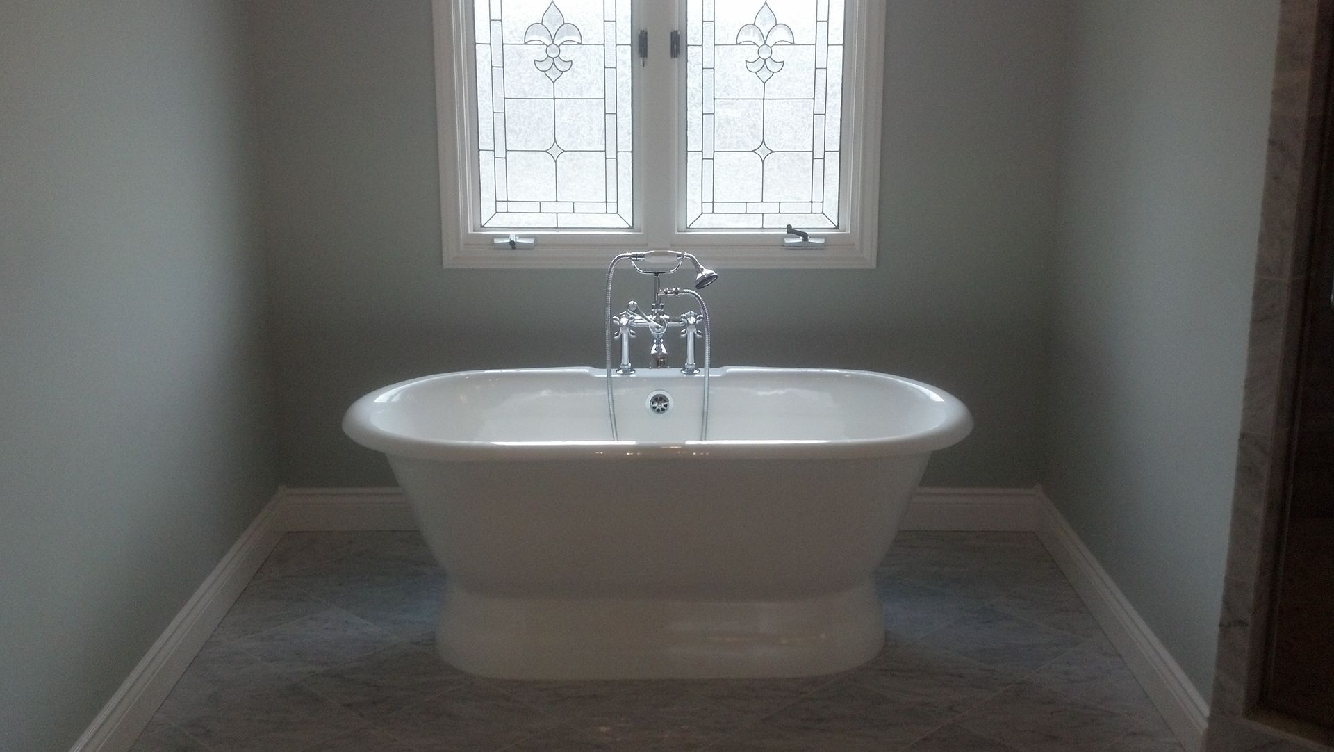 White bathtub centered beneath a frosted window in a pale green bathroom.
