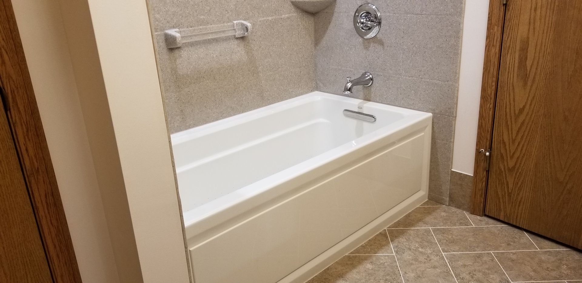 A white bathtub with a faucet, in a bathroom with stone tile walls and flooring. Wooden door on right.