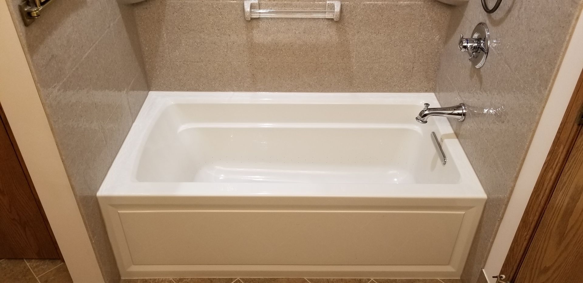 A white bathtub with a faucet and showerhead, surrounded by tan tile walls in a bathroom.