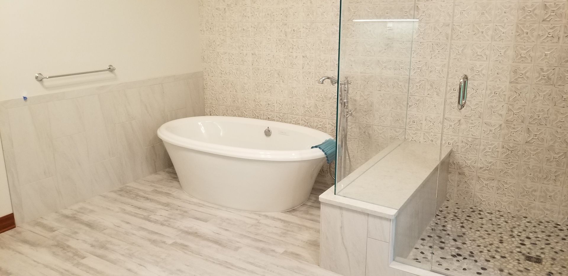Bathroom with a white oval bathtub, walk-in shower, and stone tile walls and flooring.
