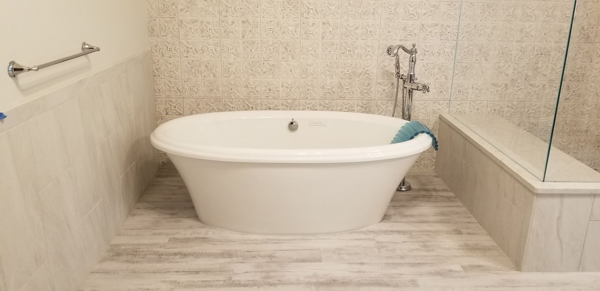 A white bathtub in a modern bathroom with a light-colored tiled floor and walls. A towel is resting on the side.