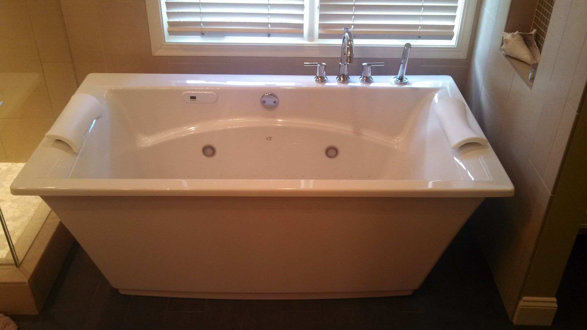 White jacuzzi tub with chrome fixtures in a bathroom, beneath a window with blinds.