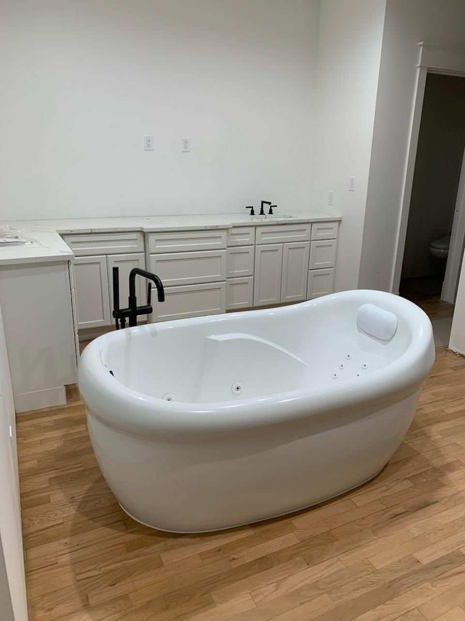 White oval bathtub in a newly renovated bathroom with wood floors and white cabinets.
