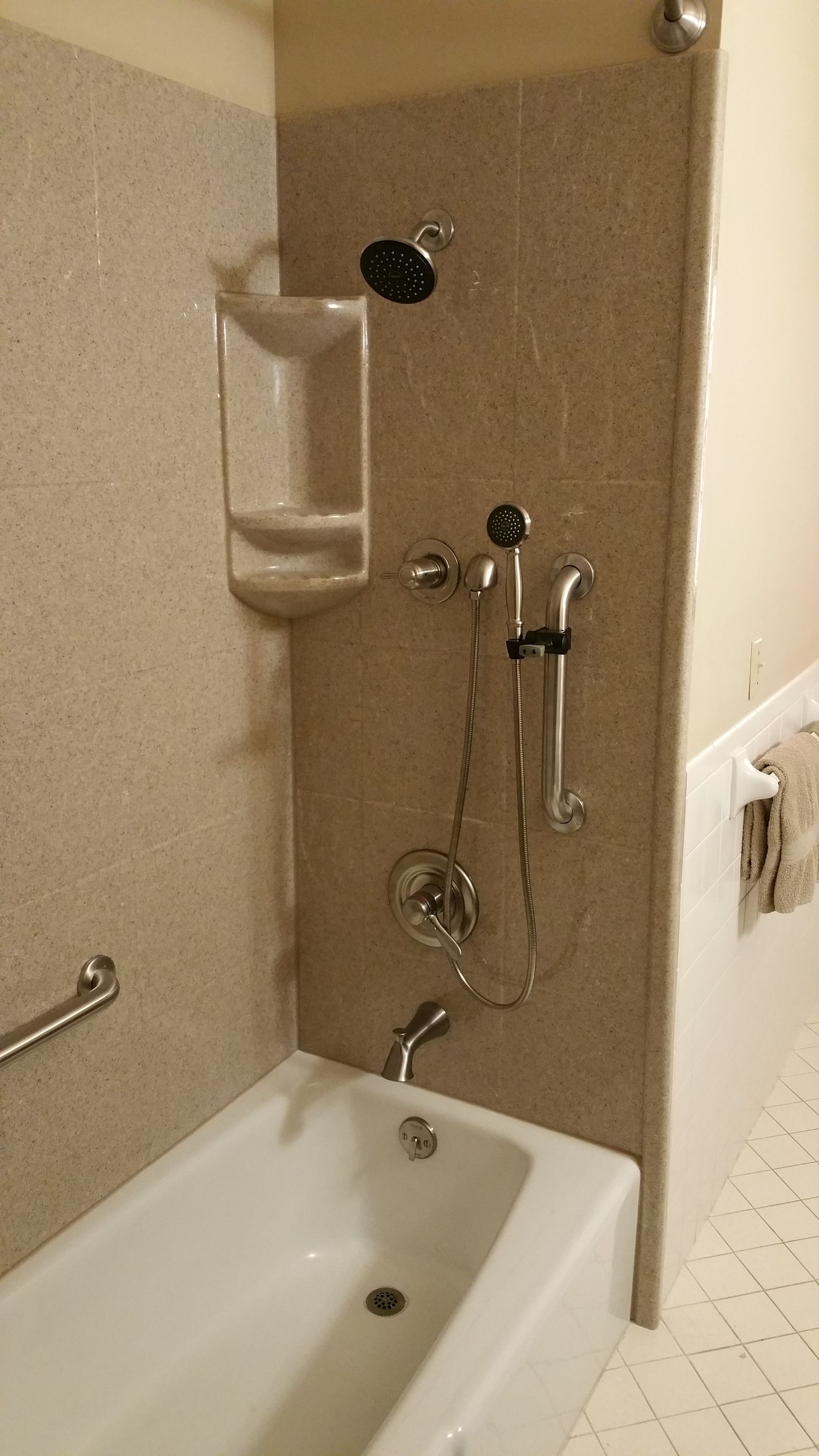 Bathroom with a white bathtub, tiled shower with showerhead and handheld wand.