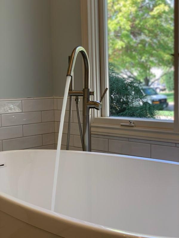 Bathtub with water flowing from a silver faucet, beside a window with a view of trees and a car.