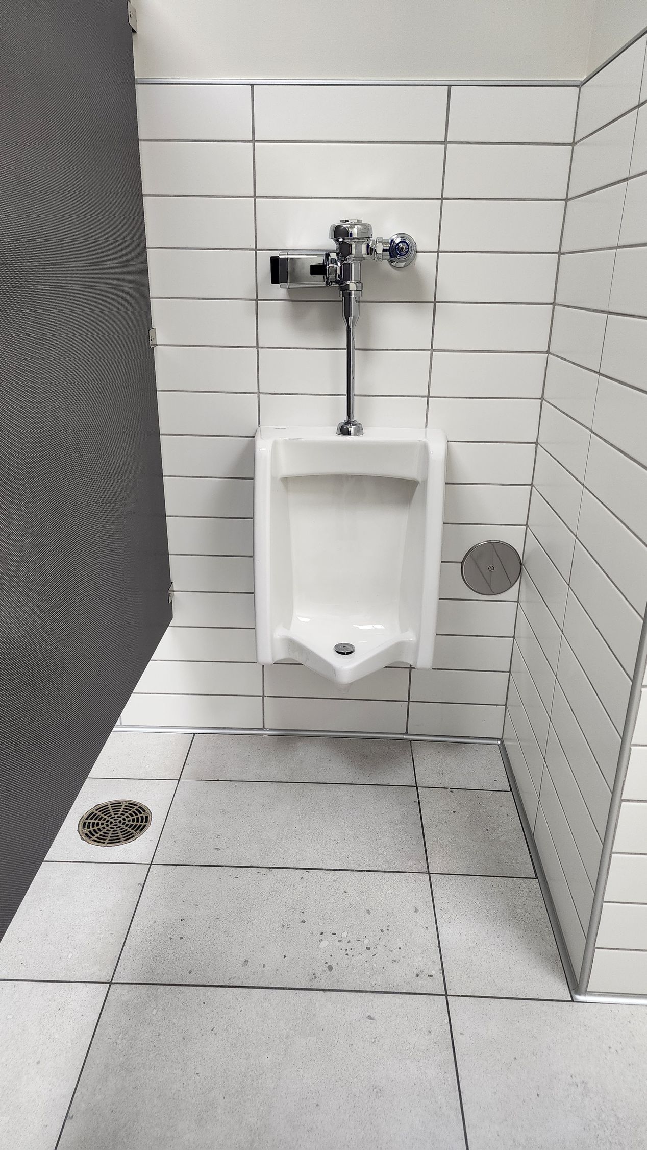 White urinal on a tiled wall in a public restroom.