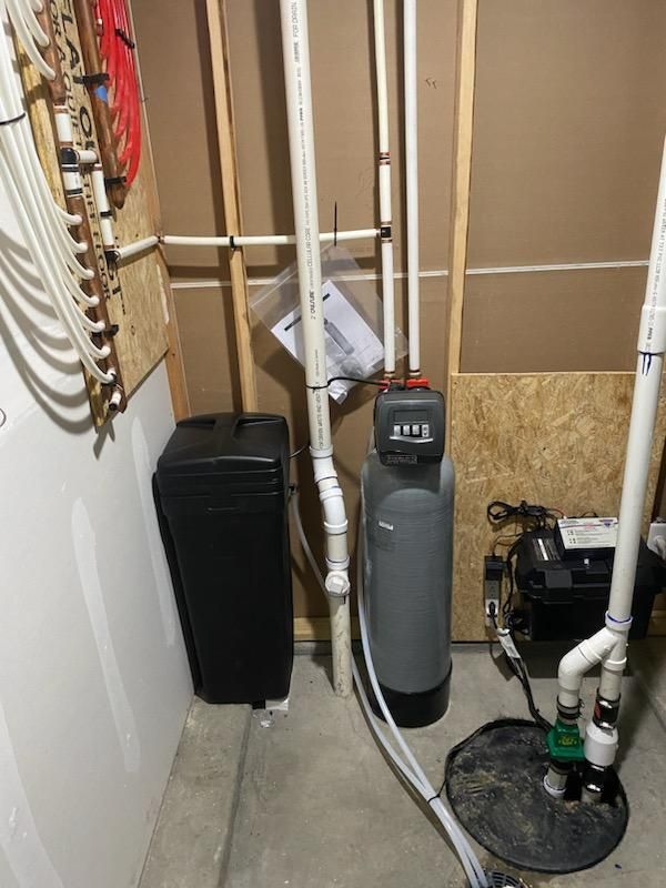 Water softener system in a basement setting with plumbing and sump pump.