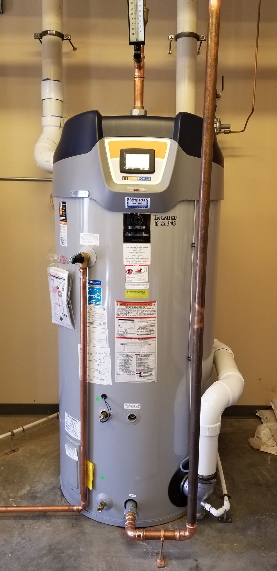 A tall, gray water heater with copper pipes in a room with tan walls.