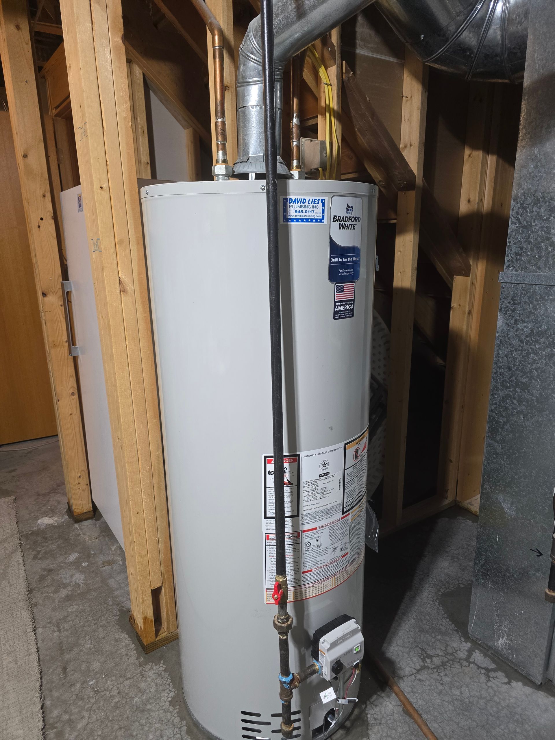 A cylindrical water heater with connected pipes and labels in a basement setting.
