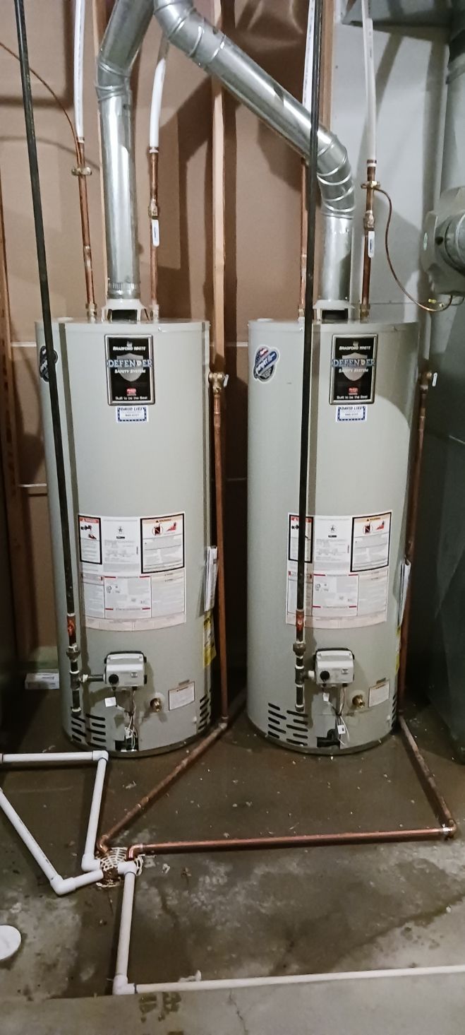 Two tall, cylindrical water heaters side-by-side with silver ventilation pipes. 