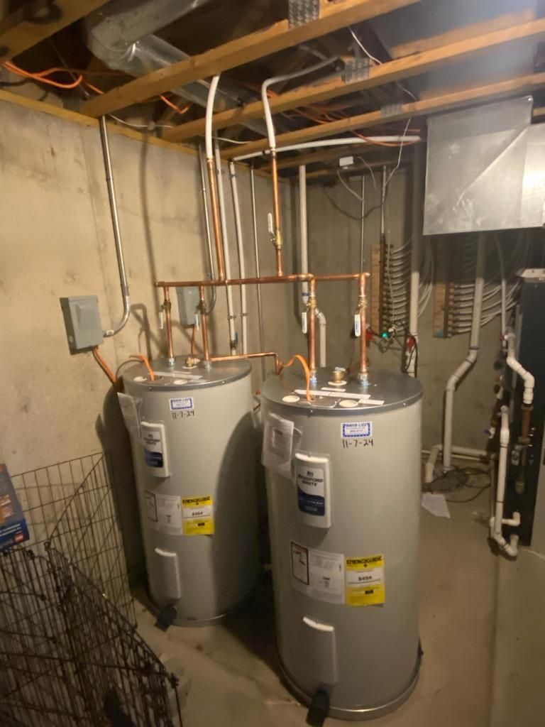 Two water heaters in a basement. Copper pipes connect to the tops. 