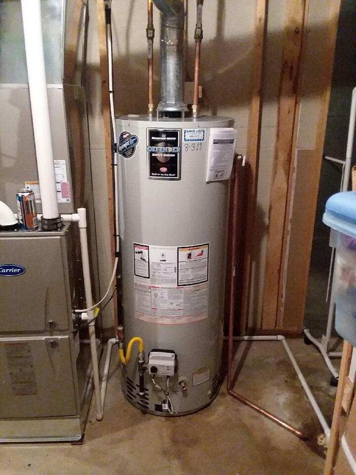 A tall, cylindrical water heater in a basement setting with copper pipes and a gas line.