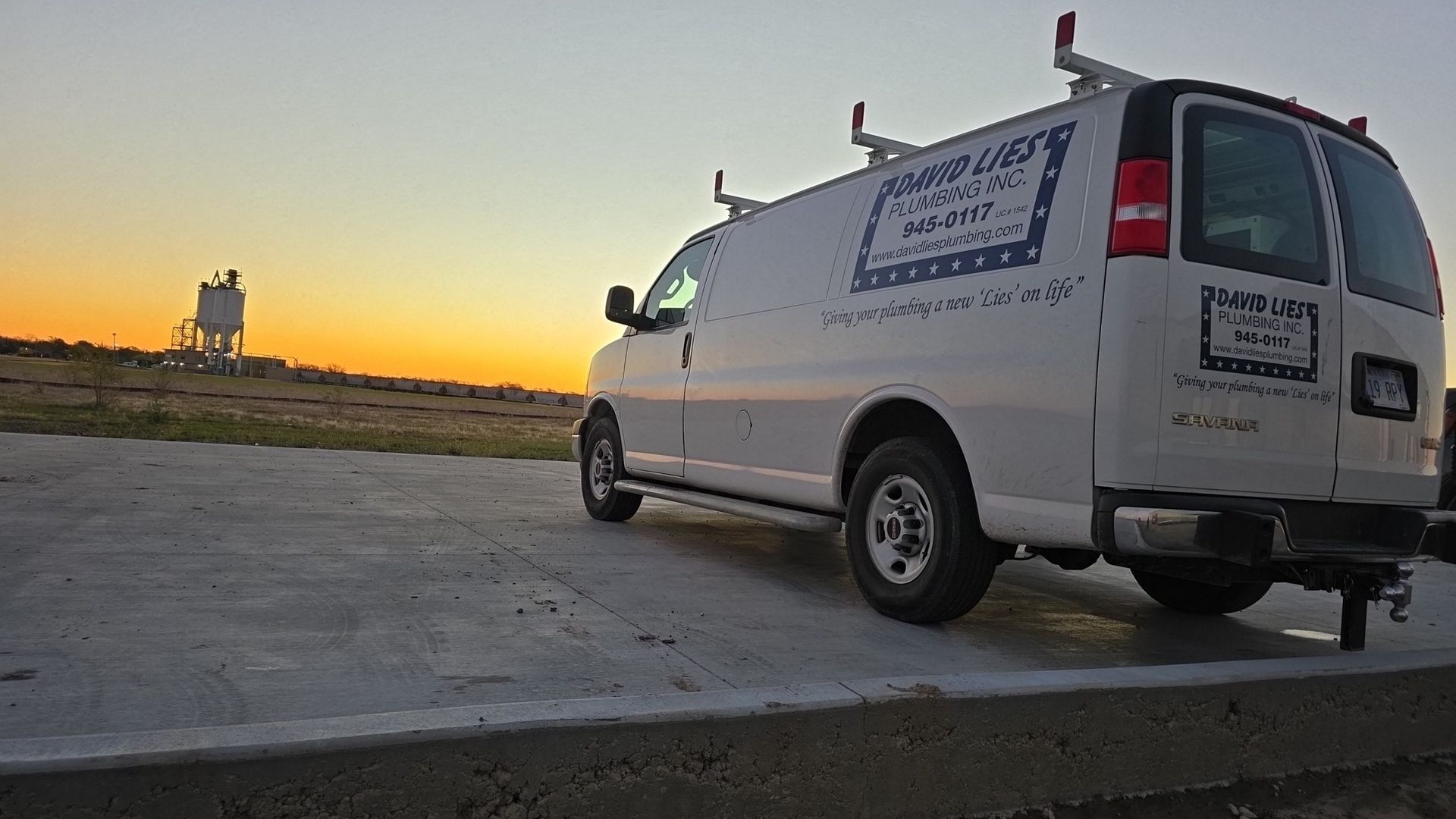 White work van parked on concrete at dusk, with equipment rack and logo.