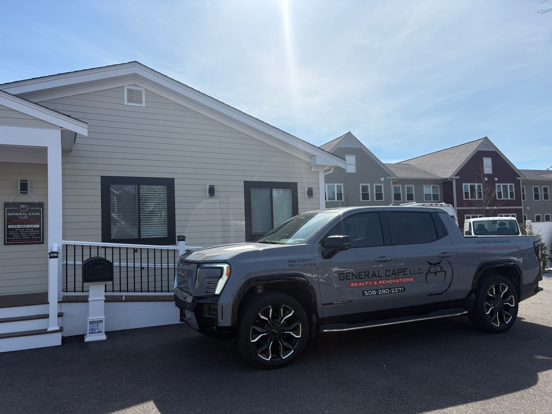 A grey GMC Hummer EV pickup truck parked in front of a light-colored building under a clear blue sky.