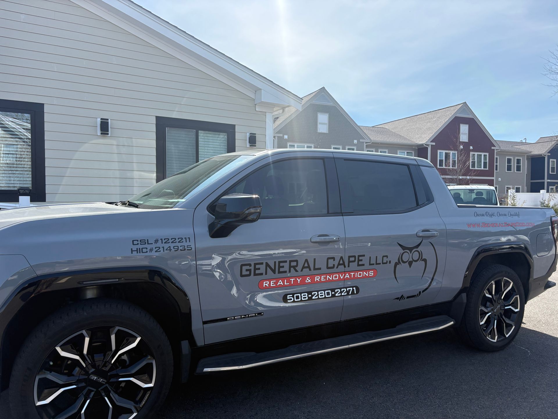 A grey GMC Hummer EV pickup truck parked in front of a light-colored building under a clear blue sky.