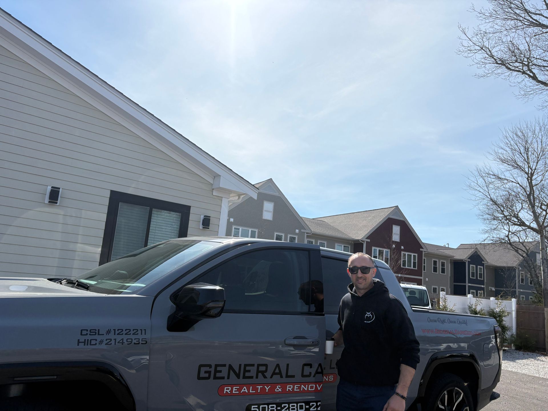 A man beside a grey GMC Hummer EV pickup truck parked in front of a light-colored building under a clear blue sky.