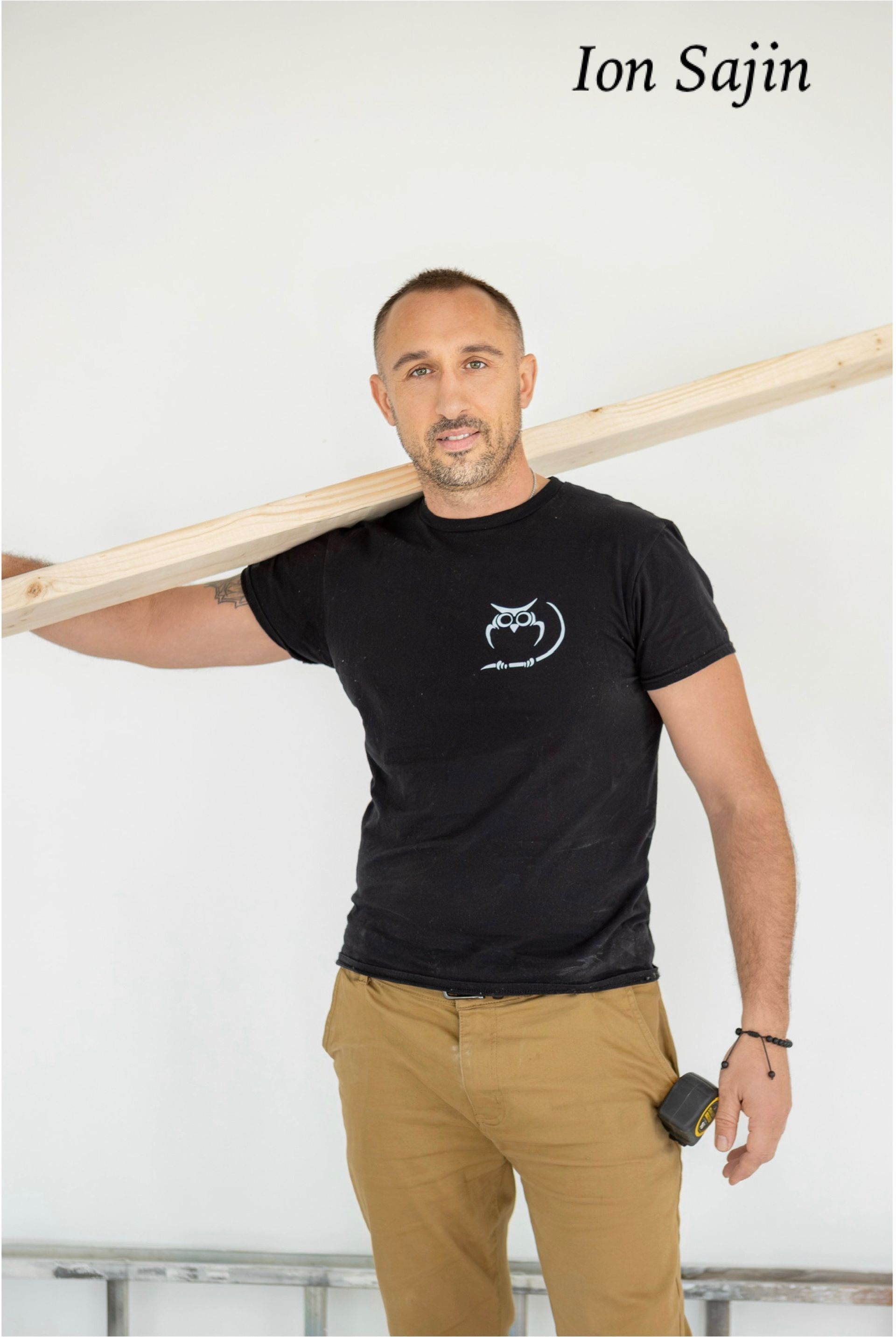 Man, Ion Sajin, wearing black shirt and brown pants, holding lumber on shoulder.