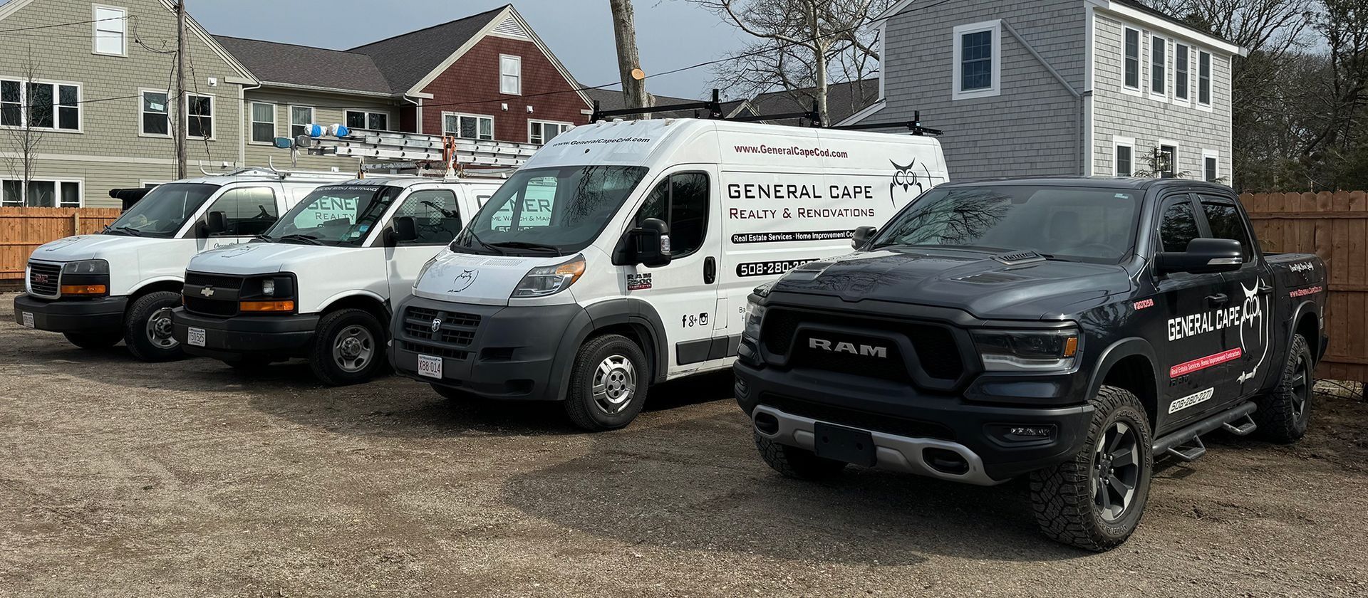 Vehicles parked in front of buildings. There are three white vans and a black truck in the foreground.
