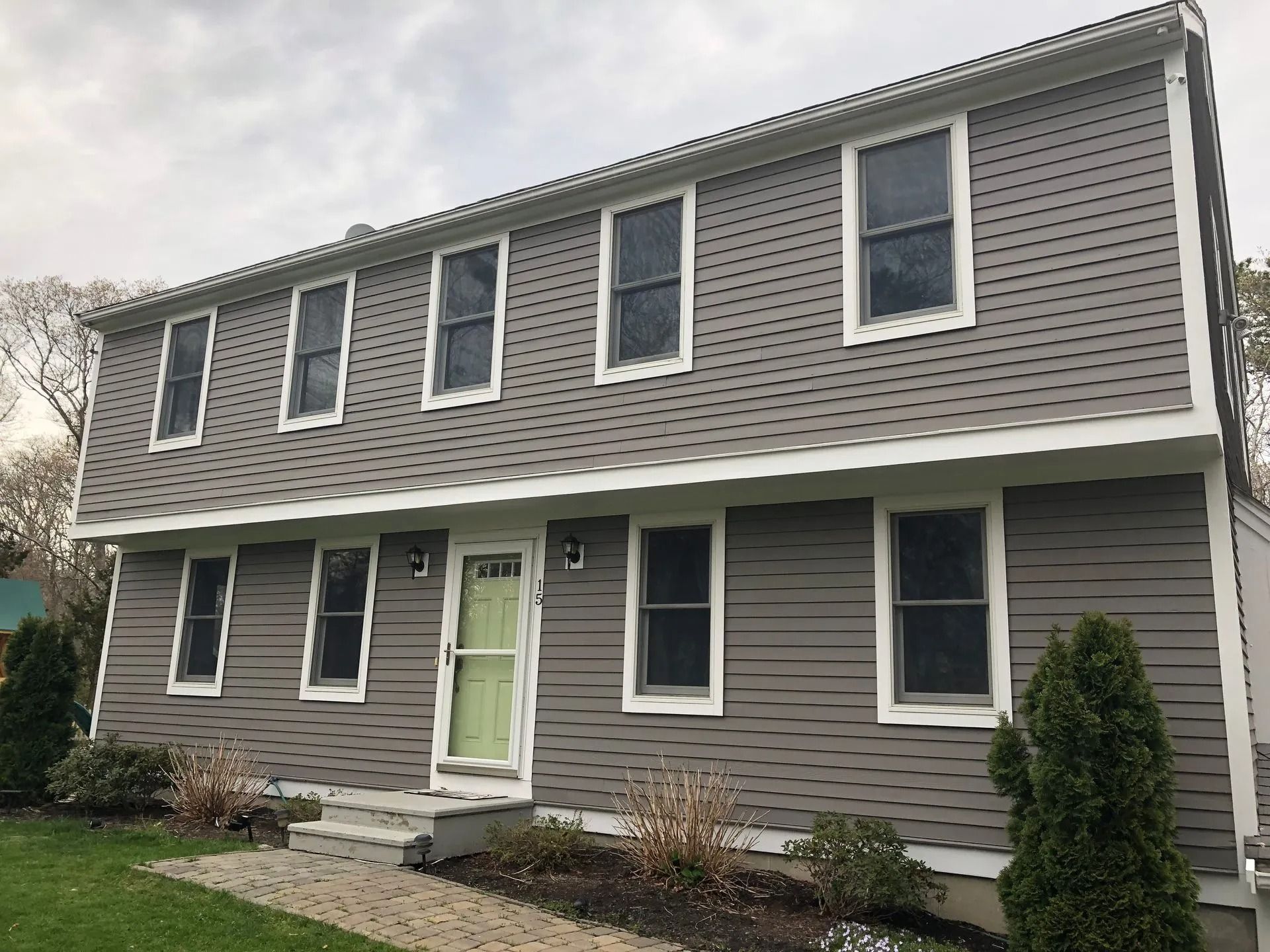 Two-story house with gray siding, white trim, and a green front door under a cloudy sky.