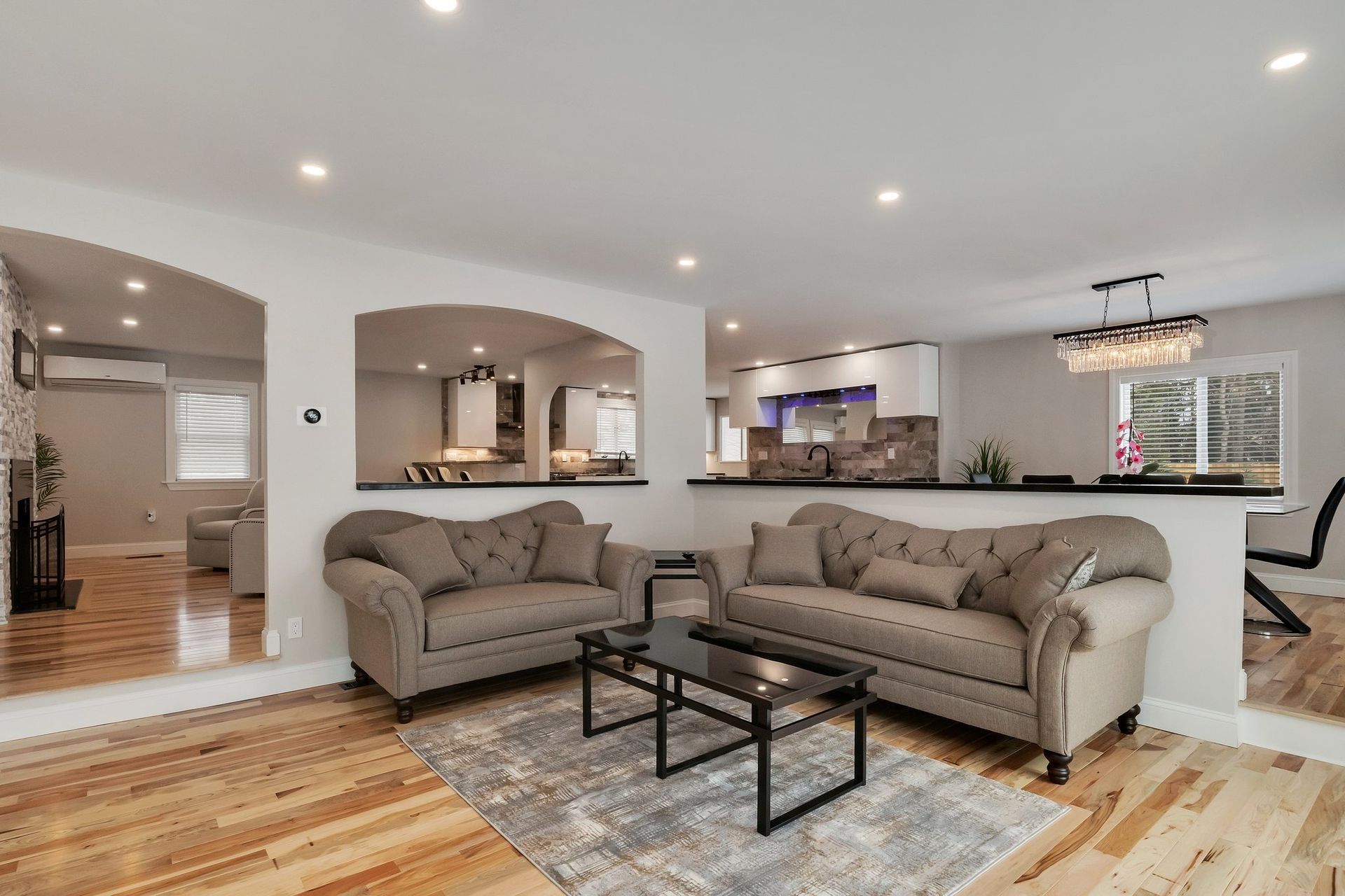 Living room with arched doorways, two gray sofas, black coffee table, open to kitchen.