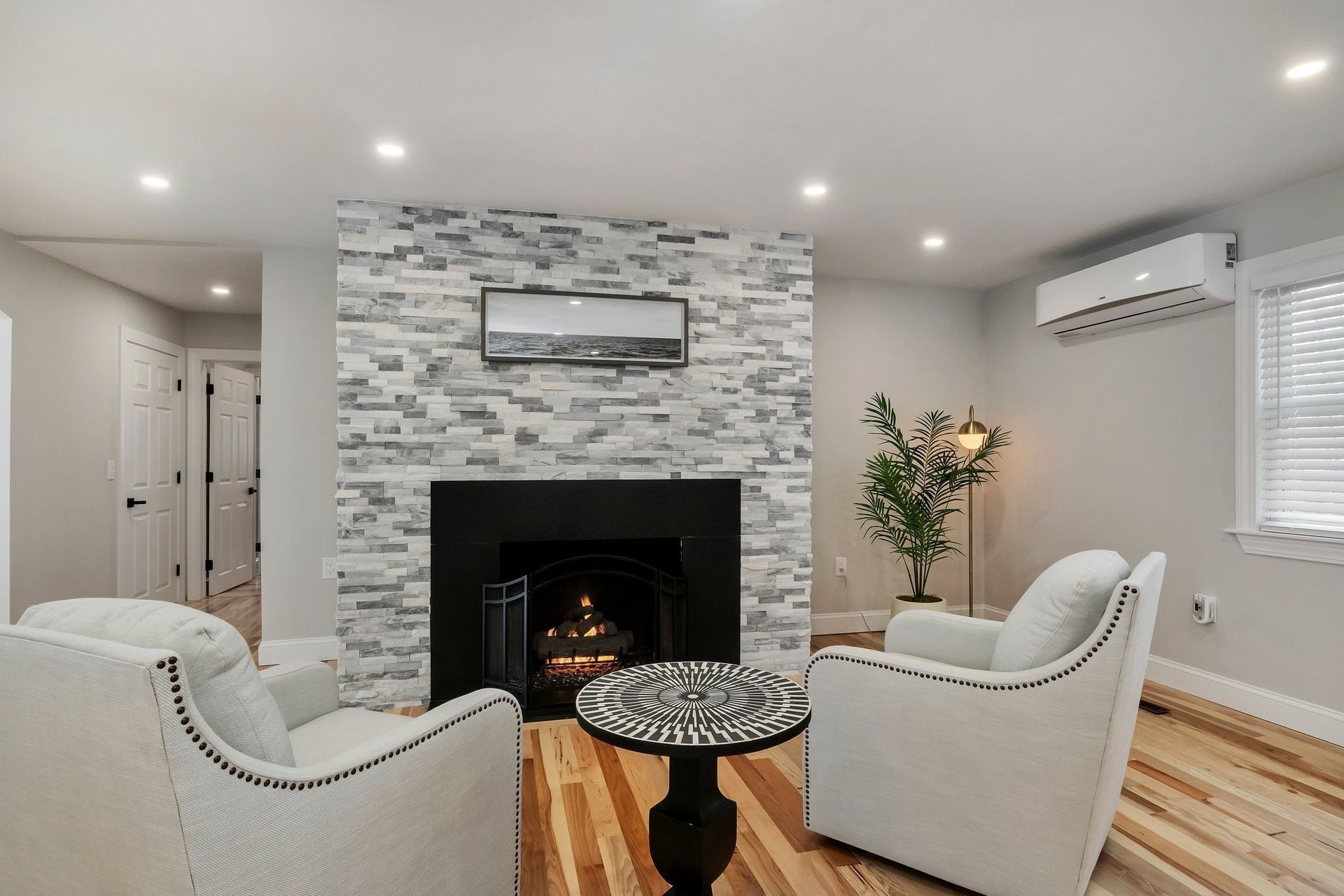 Living room with a stone fireplace, two white armchairs, and a round patterned table.