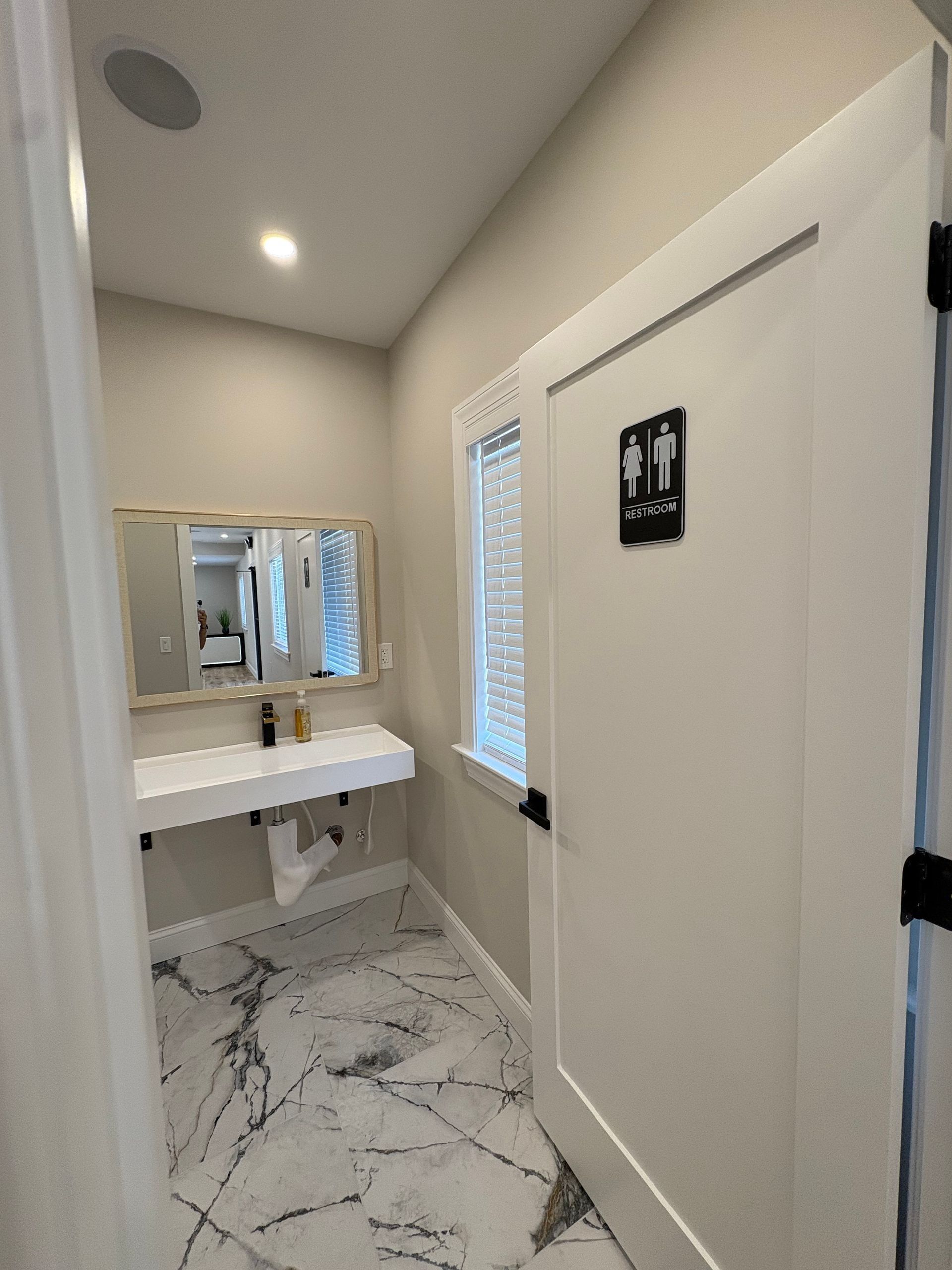 Bathroom with marble floor, floating sink, mirror, and gender-neutral restroom door.