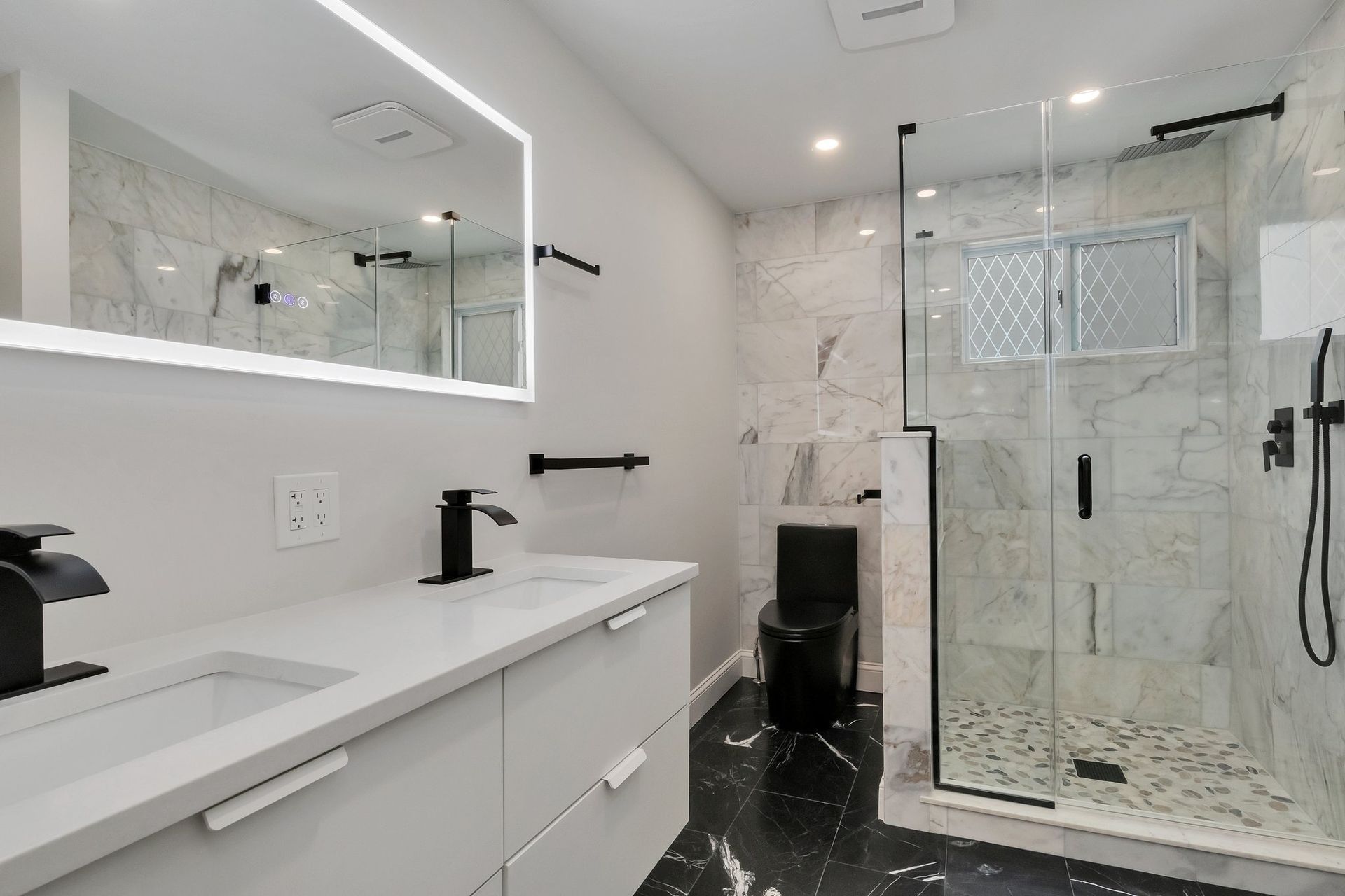 Modern bathroom with white cabinets, marble tile, and black fixtures.