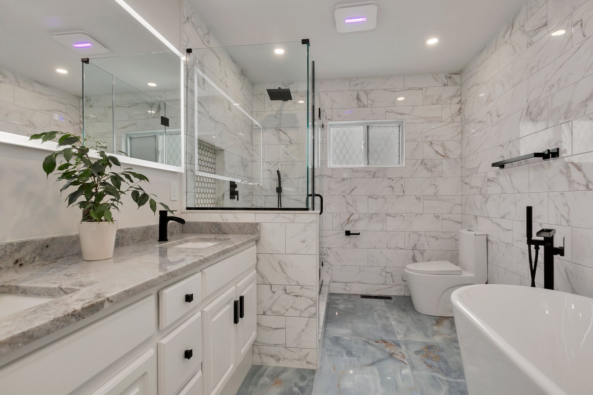 Modern bathroom with marble tile, glass shower, double vanity, and freestanding tub.