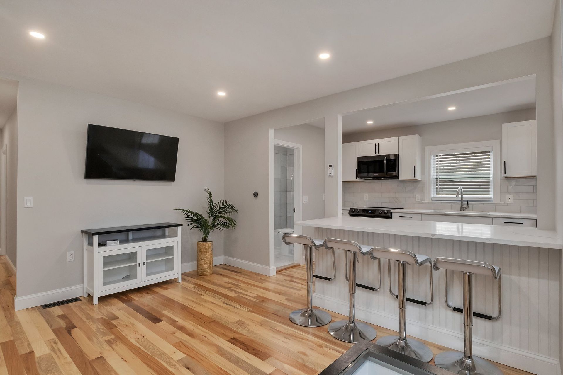 Open-concept living space with hardwood floors, a kitchen island with stools, and a TV mounted on a gray wall.
