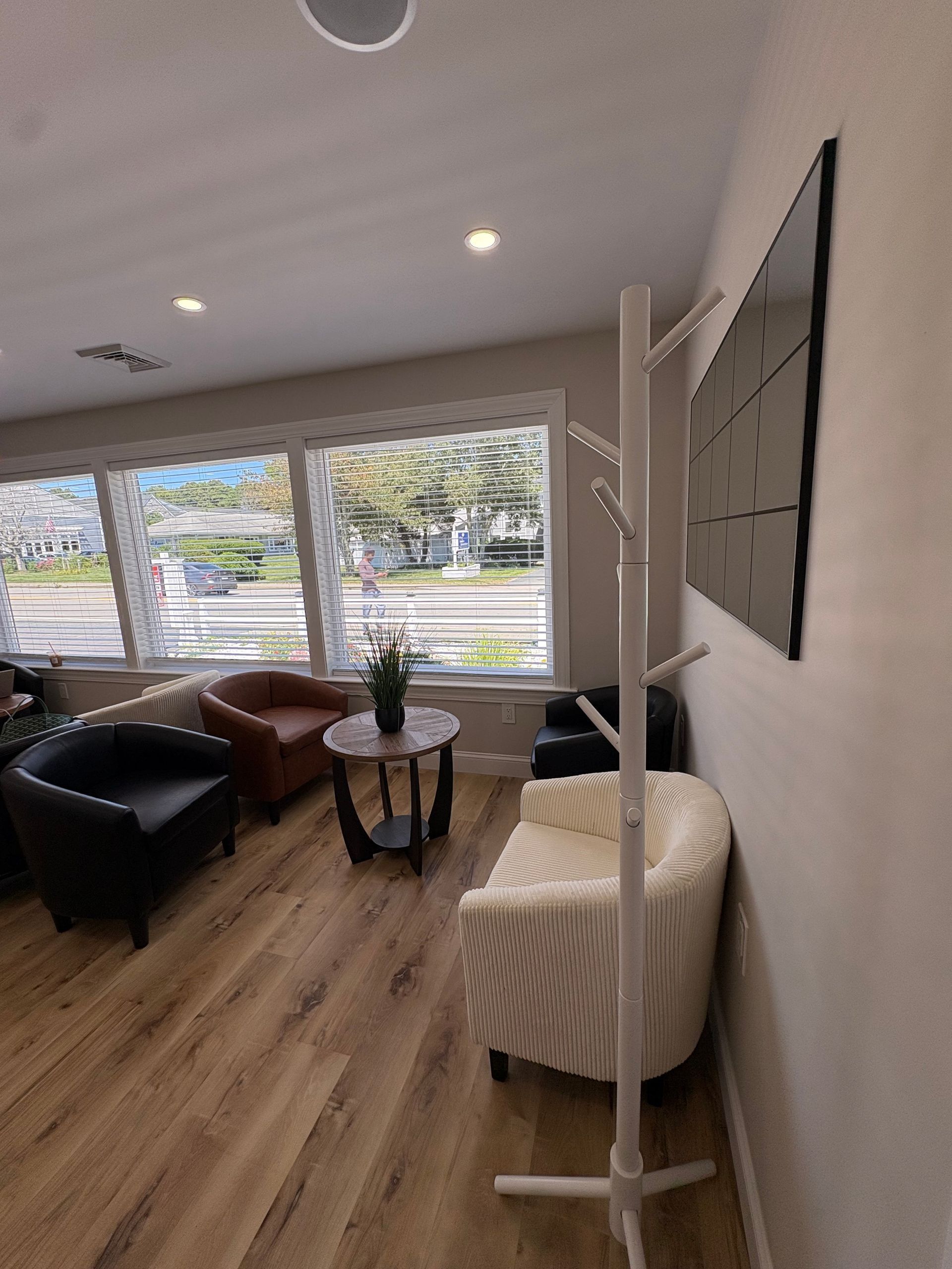 Waiting room with chairs, a table with flowers, and a coat rack by a window.