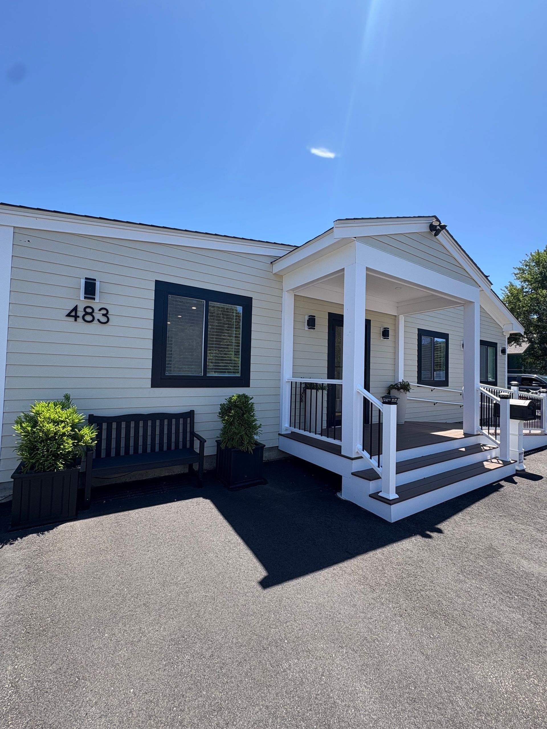Light yellow building with dark trim, porch, and number 483 on facade. Gravel parking, blue sky.
