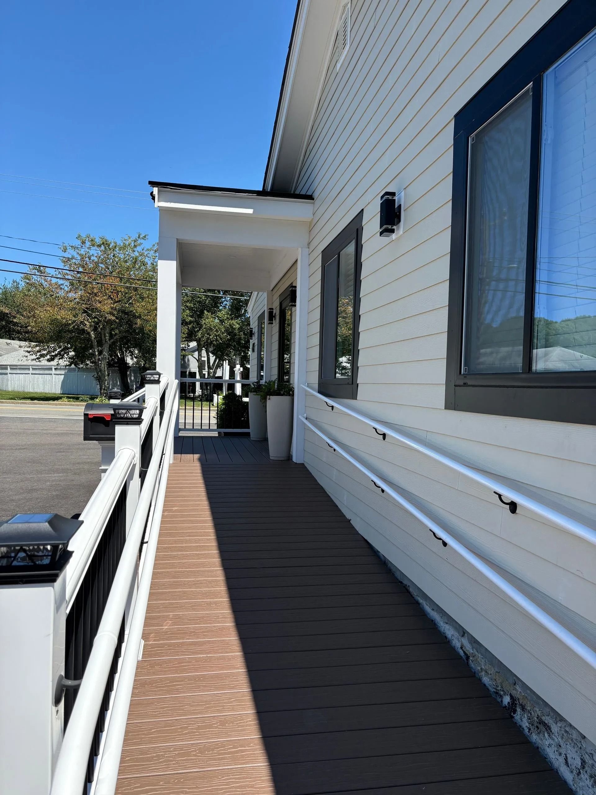 Exterior view of a white building with a wooden ramp, black-framed windows, and a covered porch.
