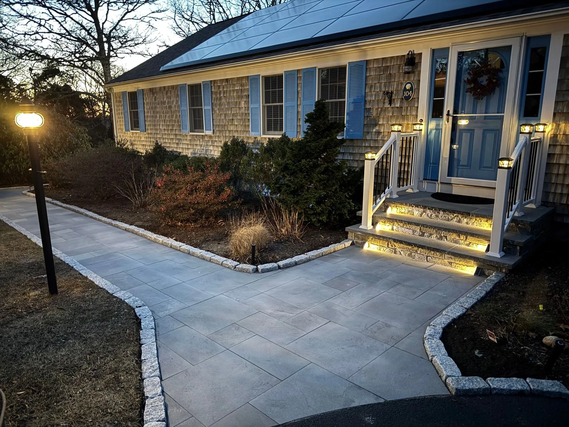 Pathway with lit steps leading to a house with blue shutters and door. Nighttime scene.