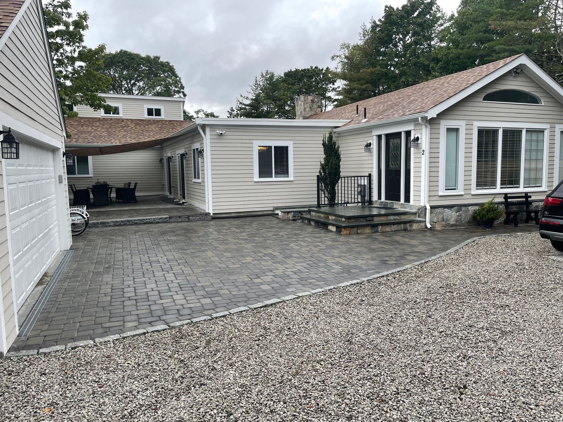 Exterior view of a house with a gray paver driveway and gravel landscaping; garage on the left.