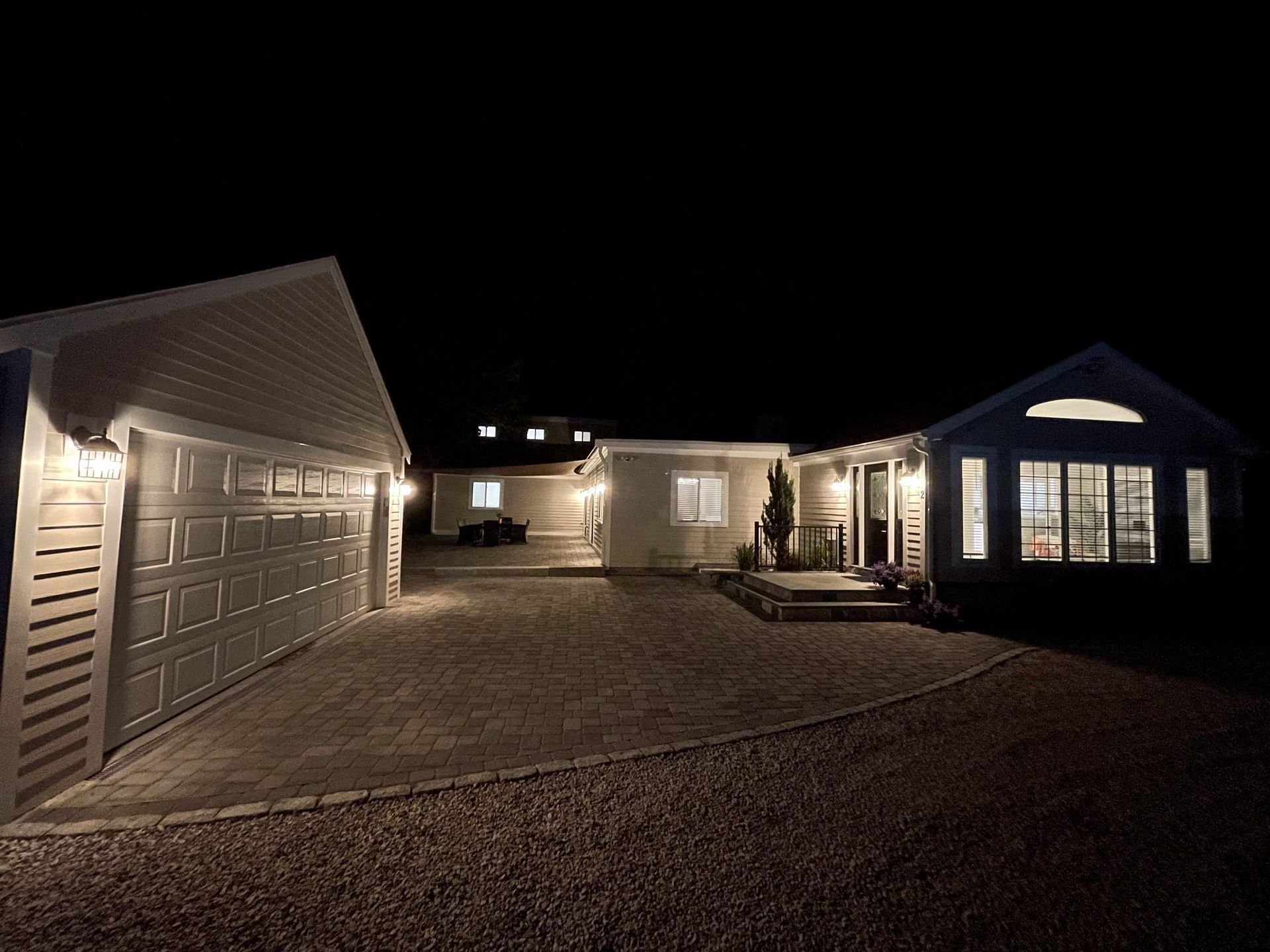 Night view of a house and detached garage with lights on, gravel driveway.