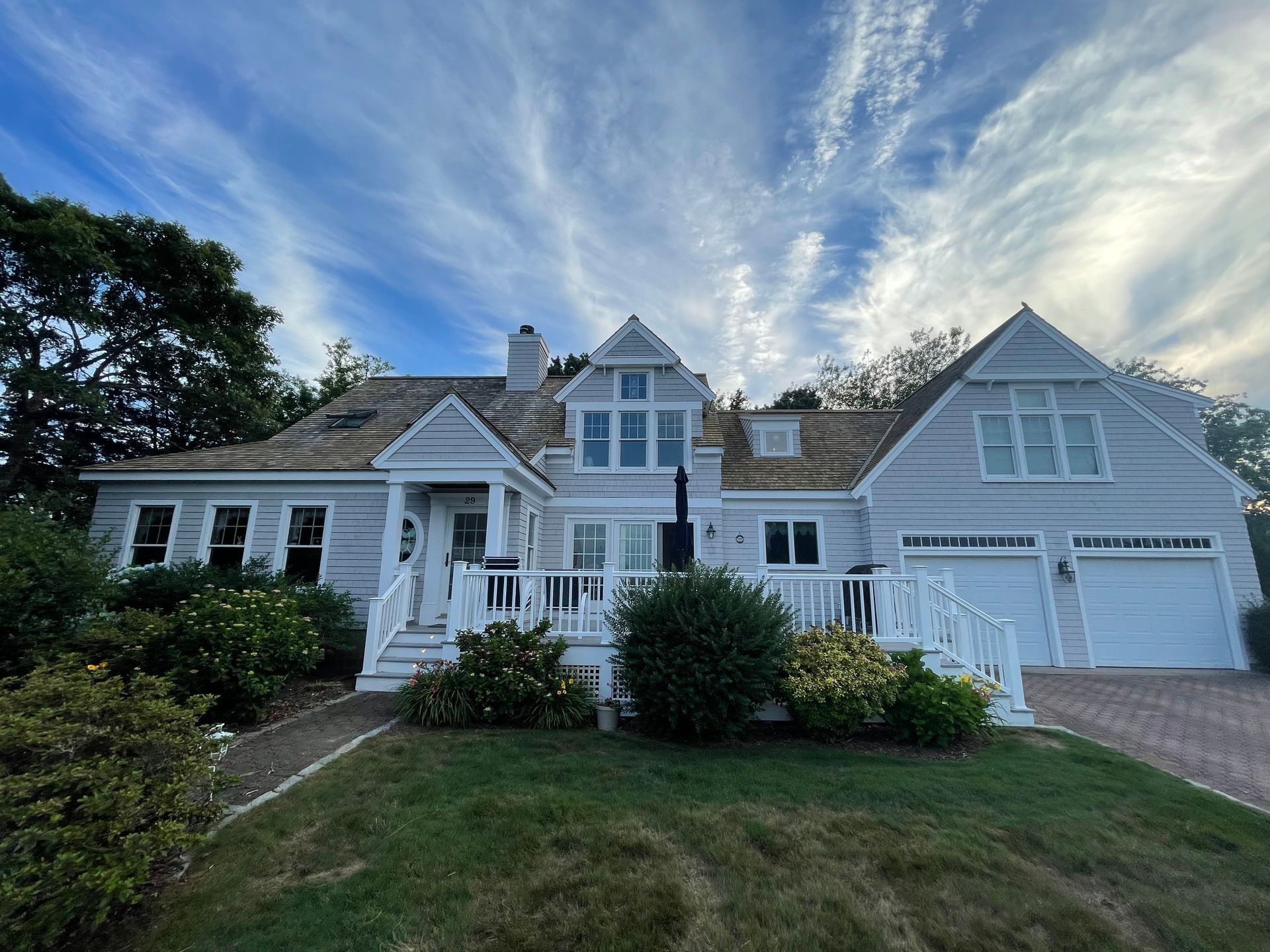 Light blue coastal home with white trim and a brown shingle roof under a cloudy blue sky.