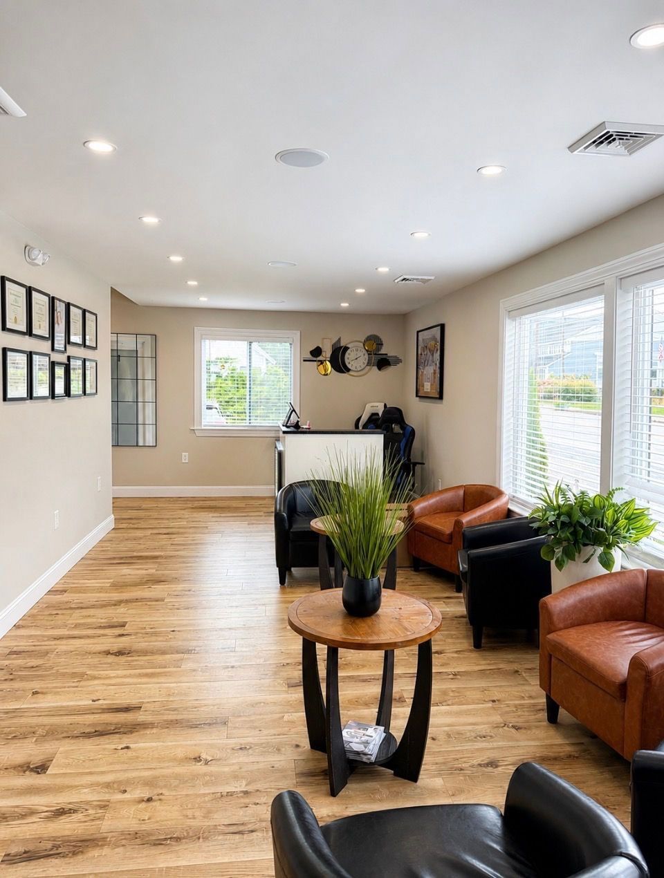 Bright lobby with hardwood floors, leather chairs, potted plants, and large windows letting in natural light