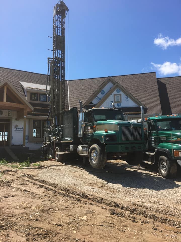 Green well drilling truck outside a building under construction on a sunny day.
