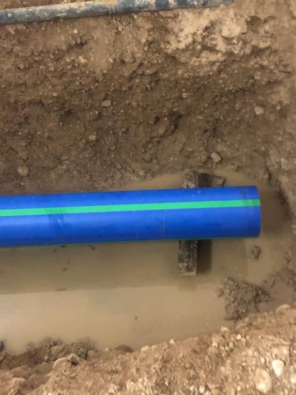 Blue pipe with green stripe in a trench. Brown soil and muddy water surround it.
