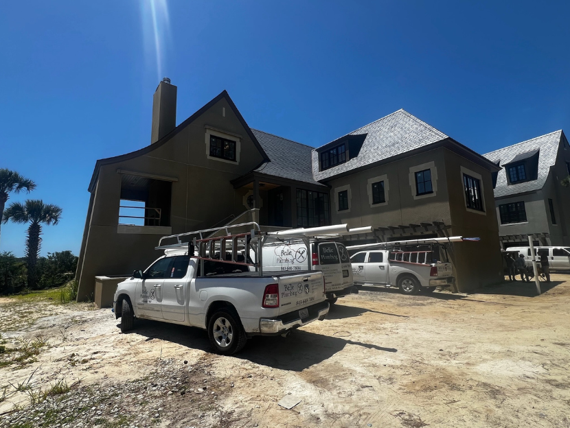 Two-story house under construction with two white pickup trucks in front on a sunny day