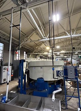 Large white industrial machine with blue base in a factory workshop, surrounded by pipes and metal framing