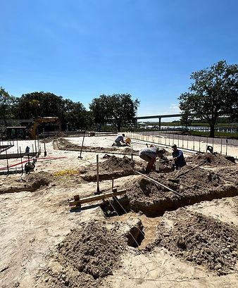 Workers digging a large outdoor foundation pit at a construction site under a clear blue sky
