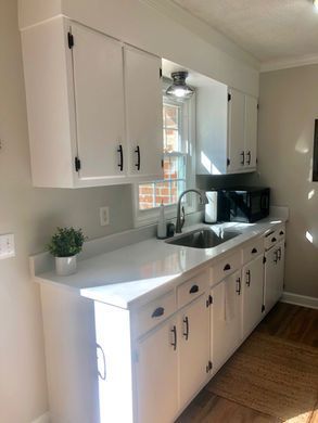 Bright white kitchen with upper cabinets, sink, black countertops, and hardwood floor.
