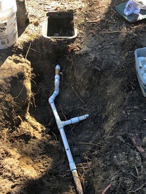 Open trench with white PVC plumbing pipes connected to a sewer line near a utility box