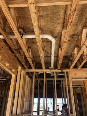 Wood-framed construction interior with exposed rafters and a white duct running along the ceiling.