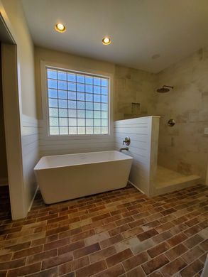 Modern bathroom with freestanding tub, glass block window, shower, and brick tile floor